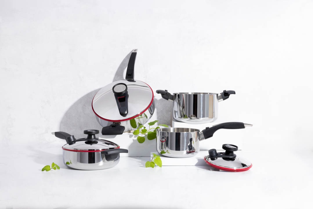 A close-up shot of a Royal Prestige cookware set on a sleek, modern kitchen countertop. The pots and pans are gleaming with a metallic shine, showcasing their high-quality construction. Steam gently rises from a pot on the stove, suggesting delicious food being prepared. The background should be a minimalist kitchen with natural light filtering through the window.